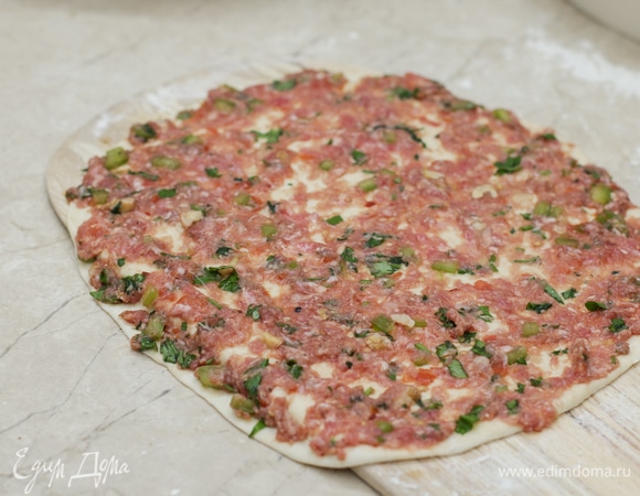 Каждый шар раскатайте в тонкий сочень. Переложите его на специальную лопаточку для пиццы или бумагу для выпечки, чтобы легче было переносить. Выложите на сочень 1–2 ст. л. подготовленной начинки и распределите фарш пальцами по всей поверхности лепешки.