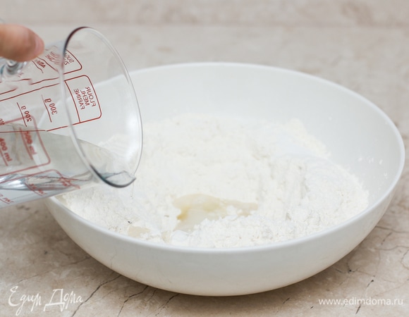 В широкой миске смешайте все ингредиенты для теста. Мука у всех разная, поэтому наливайте воду постепенно. Замесите не очень тугое тесто. Накройте миску с тестом пленкой или полотенцем и оставьте отдыхать на 10–15 минут. Здесь важно обратить внимание на температуру теста, она должна быть около 60°C.