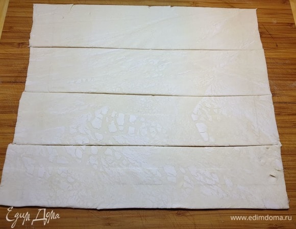 Размороженное слоеное тесто немного раскатываем и нарезаем полосками, шириной 6 см.