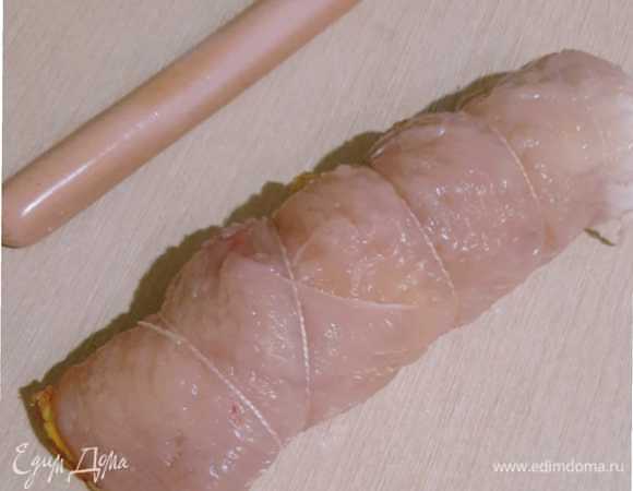 Далее на пласт филе выкладываем блинчик, сосиску. Заворачиваем в рулет, шелковой ниткой закрепляем.