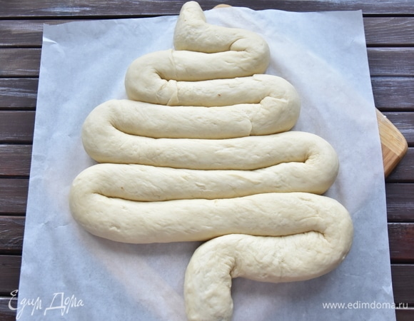 Выложить тесто швом вниз на пергаментную бумагу, формируя фигуру, похожую на елочку. Дать тесту подойти, смазать взбитым желтком, вставить подготовленные помидоры черри и маслины. Выпекать пирог в духовке, разогретой до 180°C, минут 45.