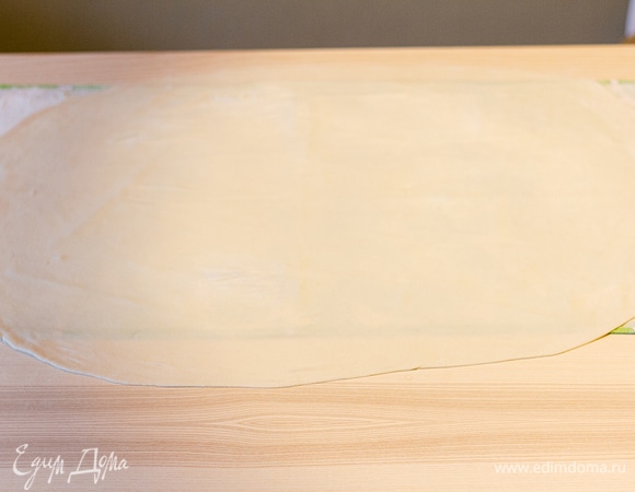 Постелите на стол полотенце и посыпьте его мукой. Немного раскатайте на нем тесто. Тесто очень пластичное, поэтому его нужно растягивать руками. Удобнее всего это делать на весу, затем постелить на полотенце и еще немного растянуть края. Если через тесто немного просвечивает полотенце, значит, достигнута идеальная толщина.