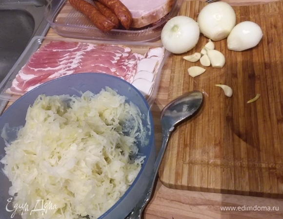 Подготовить продукты. Квашеную капусту 2 раза промыть водой, отжать. Если она крупно нарезана, то желательно ее измельчить. Мелко нарезать лук и чеснок. Колбаски нарезать кольцами, а копченую грудинку — кубиком. Так же мелко нарезать бекон. Я сразу скажу, что варила суп на мясном бульоне, но в оригинальном рецепте этого не предусмотрено. Но уверена, что так вкуснее.