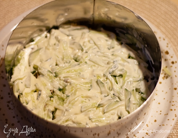 Огурцы натереть на крупной терке и немного выжать из них сок. Выложить на салат третьим слоем. Смазать майонезом.