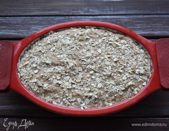 Выложить тесто в форму, смазанную растительным маслом. Сверху посыпать овсяными хлопьями. Духовку разогреть до 200°C и выпекать хлеб 40–45 минут. Дать ему немного остыть в форме, извлечь и полностью остудить на решетке.