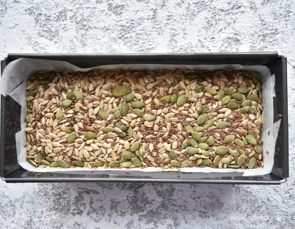 Форму для выпечки хлеба выстелить пергаментом, смазанным растительным маслом, и переложить подготовленное «тесто». Сверху густо обсыпать зерновой смесью, немного вдавив ее в «тесто». Выпекать хлеб в духовке, разогретой до 180°C, 70 минут. По истечении времени достать форму из духовки, извлечь буханку, накрыть кухонным полотенцем и оставить до полного остывания.