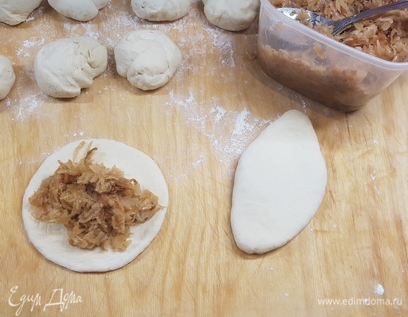 Для начинки лук мелко нарезать и обжарить на подсолнечном масле до золотистого цвета. Капусту мелко нашинковать. Я это делаю овощерезкой. Добавить капусту к луку и жарить до готовности. Посолить по вкусу. Разделить тесто на шарики. Каждый раскатать в лепешку и положить начинку. Защипать края и сформировать пирожок. Я его еще прокатываю немного скалкой, чтобы он стал плоским.