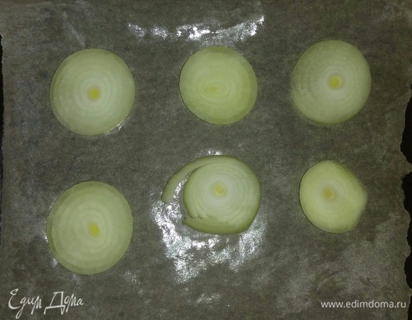 Противень, на котором будем запекать луковые штучки, застилаем пекарской бумагой и смазываем оливковым маслом. Выкладываем на него нарезанный репчатый лук.