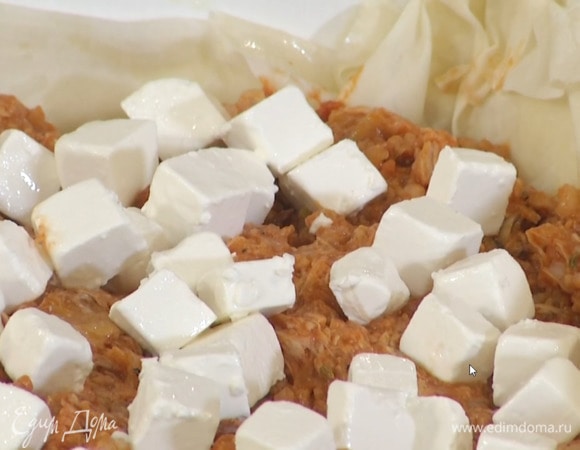 Фету нарезать небольшими кубиками, разложить на начинку, накрыть листом фило, прижать его руками и смазать маслом, затем накрыть последним листом фило, смазать его оставшимся маслом, свешивающиеся края подвернуть внутрь, на начинку.