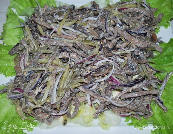 На блюдо выложите крупно нарезанный салат айсберг (половину) и сверху выложите говяжий язык с шампиньонами, огурцами и луком. А сверху — остаток салата айсберг. Полейте сверху оставшейся заправкой.