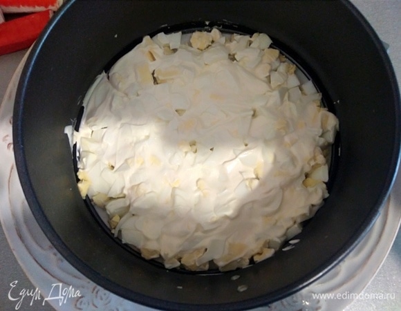 Можно просто перемешать все в миске, заправить майонезом. А можно собрать в кольце. Выглядит это празднично и красиво. Первый слой — яйцо и майонез.