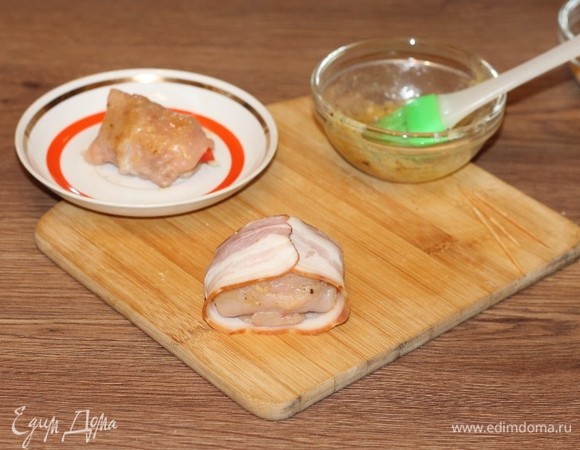 Смажьте куриные рулетики масляной смесью и заверните в полоску бекона с одной стороны.