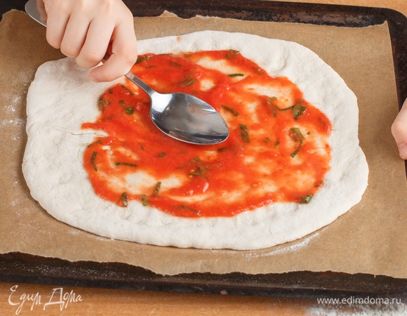 Поместить раскатанное тесто на противень, предварительно застеленный бумагой для выпечки. Выложить часть соуса и распределить его по тесту.