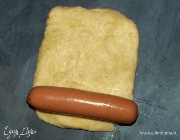 Разделить тесто на 10 частей. Каждую часть раскатать прямоугольником, на край заготовки кладем сосиску. Не надо оставлять по краям сосиски много теста.
