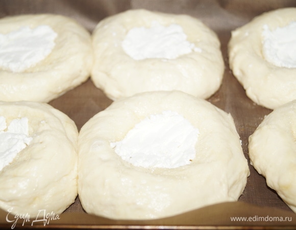 На сахарный песок выложите по 1 чайной ложке (с горкой) простого творога, разровняйте его ложкой, превратив в круг. Дайте ватрушкам отдохнуть минут 15, в это время разогрейте духовку до 220°C.