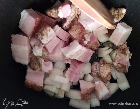 В казане разогреть растительное масло, добавить лук и нарезанную грудинку. Жарить 5 минут.