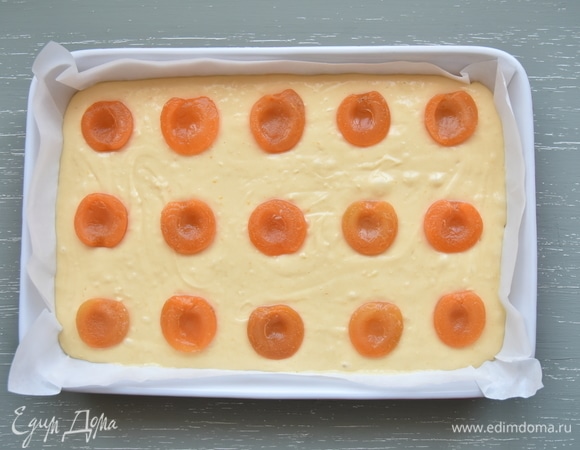 Форму для выпекания выстелить пергаментом и выложить подготовленное тесто. Разложить дольки абрикосов сверху, не вдавливая в тесто.