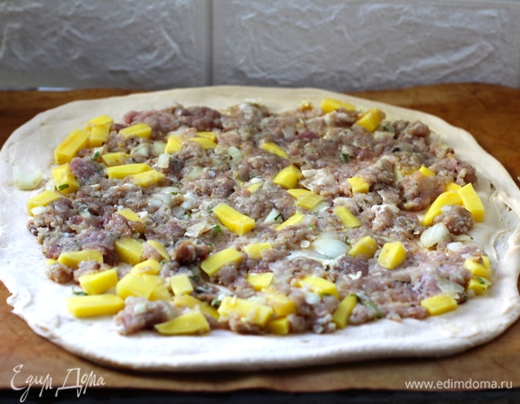 Берем одну из крупных улиток и раскатываем тонко, переносим на подготовленную застеленную форму. У меня получился круг диаметром примерно 35 см. В начинку добавляем оставшееся растопленное масло (оставим 2 ст. л. для смазки верха). Начинку делим на три части. Выкладываем одну треть подготовленной начинки, отступая от края 2–3 см.