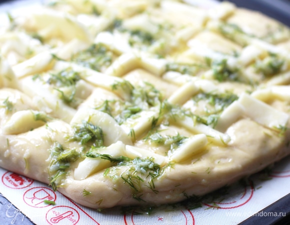 Сделать по всей поверхности надрезы (продольные и поперечные), отступив немного от краев, до половины толщины лепешки. Не прорезать тесто до конца. Разогреть духовку до 200°C. Смазать топингом поверхность.