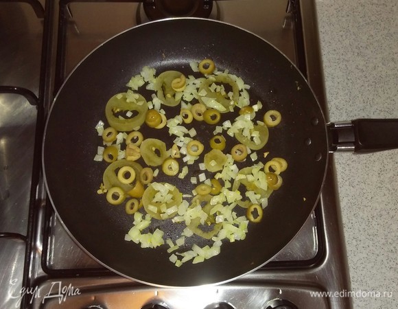 Добавляем к обжаренным кружочкам помидора репчатый лук и нарезанные оливки. Все перемешиваем и еще обжариваем на мелком огне около 1 минуты.