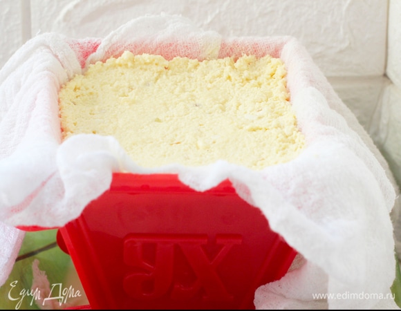 Форму для пасхи выстелить сложенной в два слоя марлей. Массу выложить в форму, поставить в тарелку и придавить сверху подходящим по форме грузом. Я взяла тяжелый четырехугольный японский салатник. Сыворотку сливать сначала часто — раз в 5 минут, потом по мере образования. Оставить так вниз головой в холодильнике до ночи перед Пасхой. Уваренная масса будет хорошо держать форму.