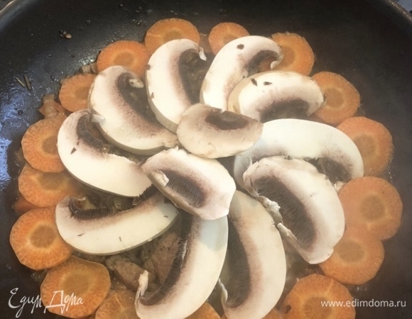 Вторую половинку моркови и оставшийся большой гриб нарезаем. Морковь — монетками, гриб — дисками. Выкладываем сверху на мясо: морковь — по краям, грибы — в центре (как на фото).