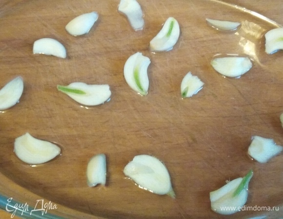 В форму для запекания налить оливковое масло. Нарезать пластинами чеснок, распределив его равномерно по дну.
