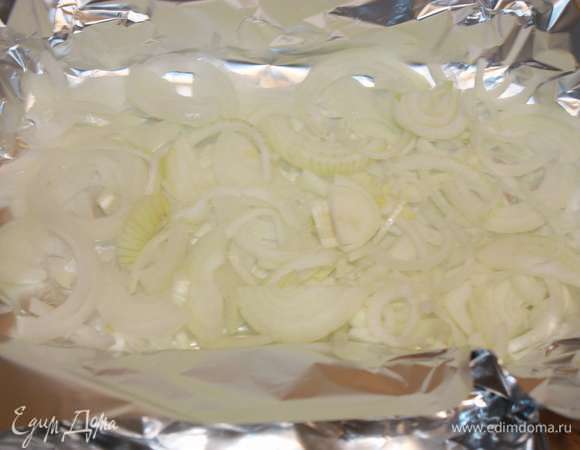 Лук нарезать. Затем берем лист фольги и выкладываем большую часть нарезанного лука.