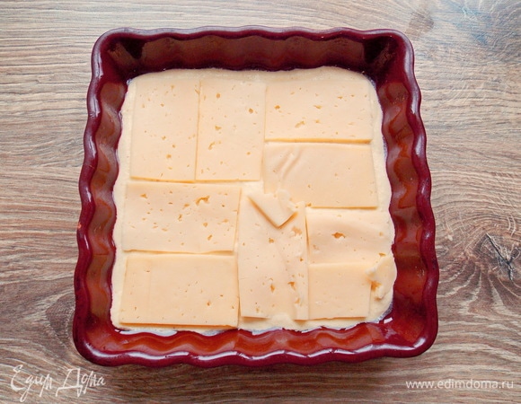 Форму 15х15 смазываем растительным маслом и выливаем 1/3 теста, разравниваем. Твердый сыр нарезаем тонкими полосками и раскладываем по всей поверхности теста.