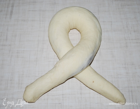 Раскатайте жгут. Заверните края, возьмите правую сторону и перекрестите, переверните вверх хвостики теста.