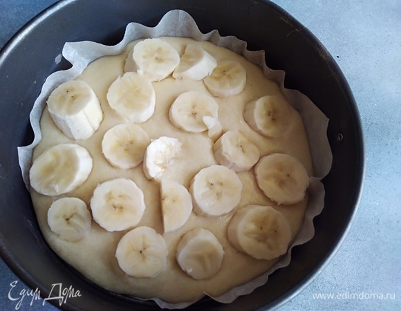 Форму выстелить бумагой для выпечки, вылить половину теста. Крупный банан нарезать кружками и разложить по тесту.
