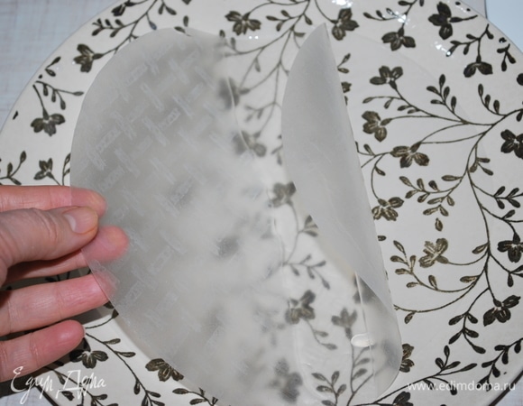 В тарелку налейте теплую воду, возьмите лист рисовой бумаги и окуните его на 8–10 секунд, чтобы он не сильно размяк.