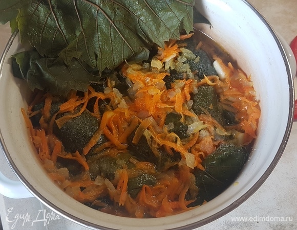 На широкий край виноградного листа выложить немного фарша и скрутить наподобие голубца. Складывать долму в кастрюлю на виноградные листья, плотно прижимая друг к другу. Обжарить лук и морковь до мягкости. Выложить сверху на рулетики. Залить водой и вином. Закрыть виноградными листьями. Поставить на огонь и дать закипеть. Попробовать на соль и, если надо, досолить. Огонь уменьшить до минимального и тушить долму 1,5 часа. Подавать с натуральным йогуртом, в который предварительно натереть чеснок.