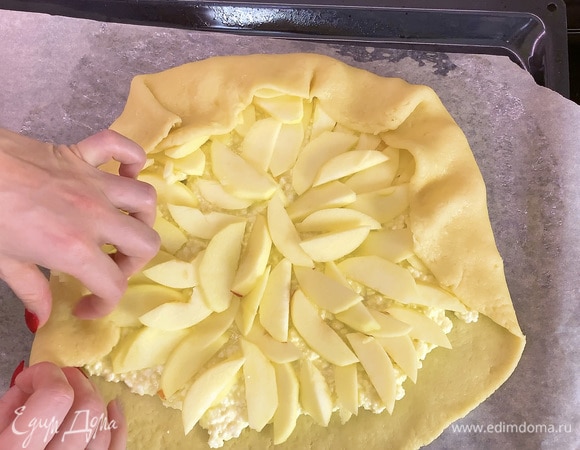 Творожную начинку кладем в центр раскатанного теста и расплющиваем так, чтоб края оставались «голыми», и сверху выкладываем пластинки яблок. Края теста завернуть внахлест и посыпать пирог сахаром.