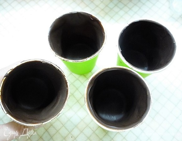 Теперь собираем наш десерт. В одноразовые бумажные стаканчики объемом 250 мл (именно бумажные, брала самые дешевые) наливаем шоколад (я использовала темный темперированный шоколад, темперирую методом простого посева), поворачиваем стаканчик по кругу, чтобы равномерно распределить шоколад. Переворачиваем стаканчики минут на 5 на решетку, чтобы стекло лишнее, затем убираем в холодильник на 15–20 минут, чтобы шоколад застыл.