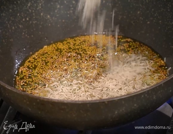 На разогретую сухую сковороду вок высыпать семена горчицы и кориандра и прогревать их пару минут, затем влить оливковое масло, всыпать рис, перемешать и дать ему пропитаться ароматным маслом.