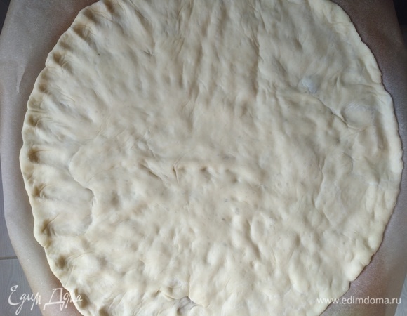 Спустя 45 минут тесто готово. У нас будет 2 пиццы. Тесто делим пополам. Руками растягиваем тесто на пергаментной бумаге, образуя круг, предварительно капнув на нее немного оливкового масла (руки тоже можно смазать маслом).
