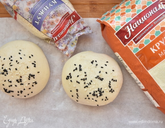 Через час подошедшее тесто разделить на части массой примерно 105 граммов. Подкатать каждый кусочек в гладкий колобок, выложить заготовки на противень, выстеленный пергаментом. После того как булочки подойдут, смазать верх крепко заваренным чаем с сахаром и обсыпать кунжутом.