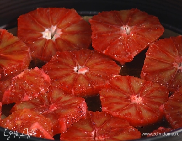 Разъемную форму застелить бумагой для выпечки, влить и равномерно распределить карамель, затем плотно уложить ломтики апельсинов и покрыть их тестом.