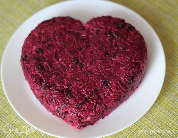 Свеклу смешать с черносливом и также добавить чесночный майонез. Это будет третий завершающий слой. Распределить свеклу по всей поверхности салата и сформировать сердечко. Удобно делать это лопаткой. Грецкие орехи положить в кулек и прокатать скалкой до мелкой крошки. Я насыпаю орехи по всему периметру сердечко из орешков. Можно просто посыпать орехами или добавить их в свеклу, на ваше усмотрение.