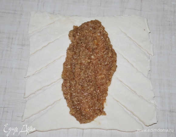 Раскатайте слоеное тесто (у меня покупное слоеное тесто), разрежьте его на квадраты. С двух сторон разрежьте тесто на полоски, на середину квадрата выложите начинку. Из этого количества теста получилось 8 штук.