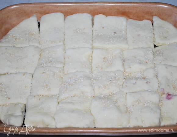 На ягоды выложите тесто, нарезанное на квадратики. Тесто тонко раскатывать не надо. Смажьте его сверху яичным желтком (при желании посыпьте кунжутом) и поставьте пирог в разогретую до 170°C духовку на 40–45 минут, выпекайте до готовности теста.