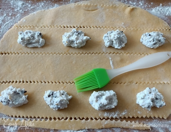 Выложить начинку небольшими порциями на расстоянии 4–5 см друг от друга. Слегка смочить кулинарную кисть в воде и промазать края теста.