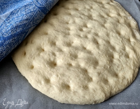 Противень застелить пергаментной бумагой. Выложить тесто, придать форму круга, сделать пальцами небольшие ямочки-углубления. Накрыть и оставить на 30 минут в теплом месте.