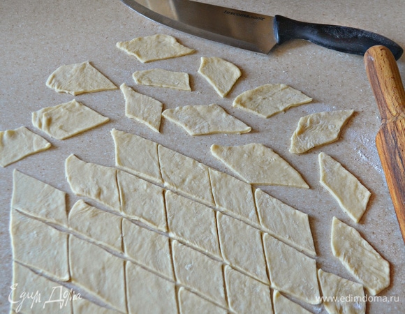 Выложить тесто на стол, слегка припыленный мукой. Раскатайте тесто в прямоугольный пласт толщиной 3–5 мм и нарежьте с помощью ножа небольшими ромбиками.