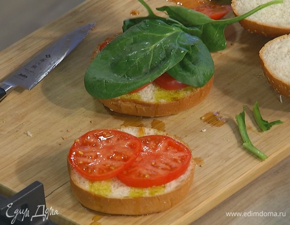 Помидор нарезать кружками, выложить на нижнюю часть булочек и накрыть листьями шпината.