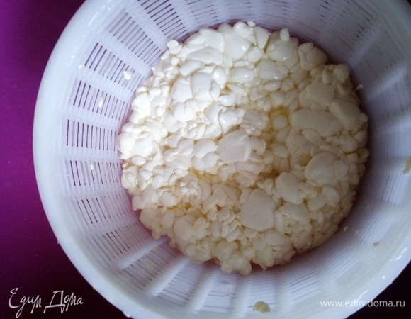 Слейте сыворотку настолько, чтобы ее слой лишь слегка покрывал слой сырного зерна. Аккуратно разложите сырное зерно в форму при помощи шумовки (или, как у меня, ложка-лопатка для сырного зерна). Сырное зерно сначала полностью не влезет в форму, можно слегка утрамбовать сырную массу в форме чистыми руками. На этом этапе вы можете внести различные добавки по вашему желанию: травы, паприку резаную, томаты, оливки. Мы же не любим сыр с добавками.