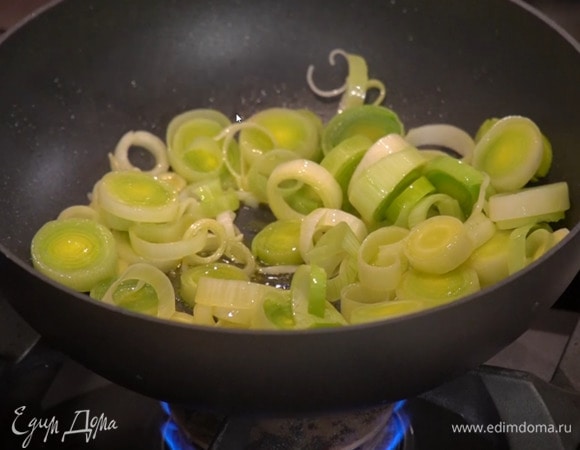 Разогреть в сковороде вок оливковое масло и обжарить лук-порей до прозрачности.