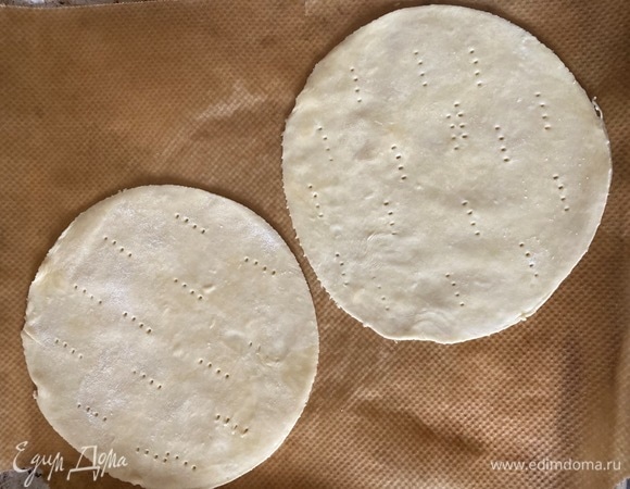 Достаем по одному шарику, тонко раскатываем, тарелкой вырезаем круг (диаметр — 20 см), делаем вилкой частые наколы и отправляем в разогретую до 200°C духовку. Я выпекала сразу по два коржа.