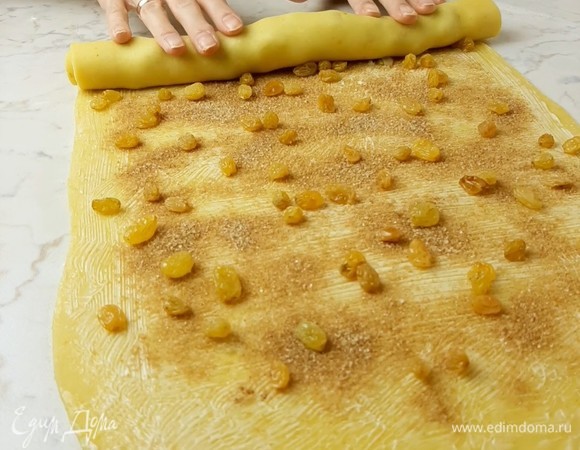 После того как тесто подойдет, раскатываем его в прямоугольник размером примерно 30 х 45 см. Смазываем сливочным маслом комнатной температуры. Посыпаем смесью сахара и корицы. Выкладываем равномерно изюм или цукаты. Скручиваем в плотный рулет и оставляем минут на 15.